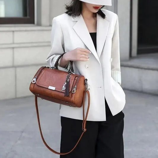 Mulher com blazer branco e roupa preta segurando a bolsa Seline caramelo pela alça de mão.